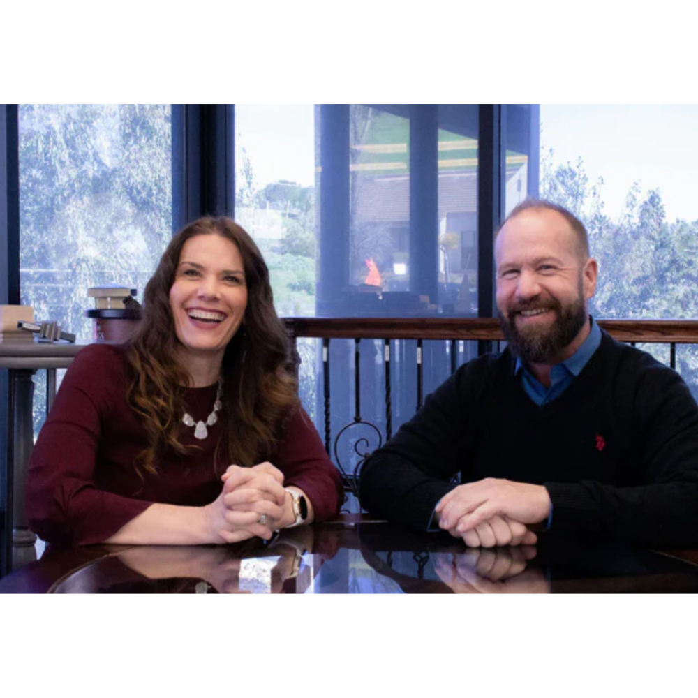 Two people sitting at a table with a window view of trees and buildings.